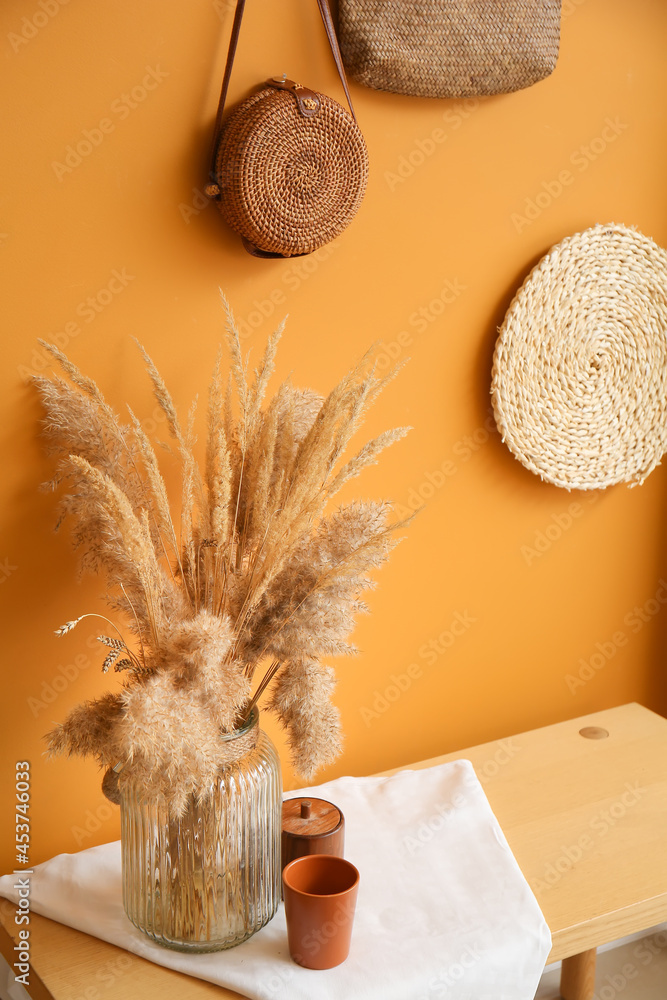 Stylish vase with cup on table near color wall