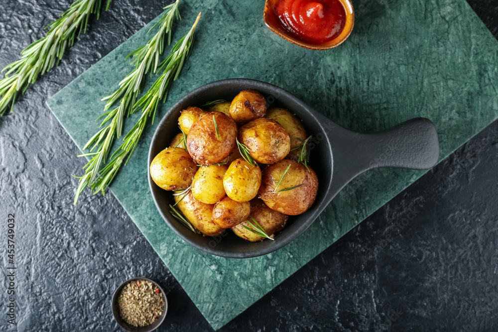 Frying pan with baked potatoes and rosemary on dark background