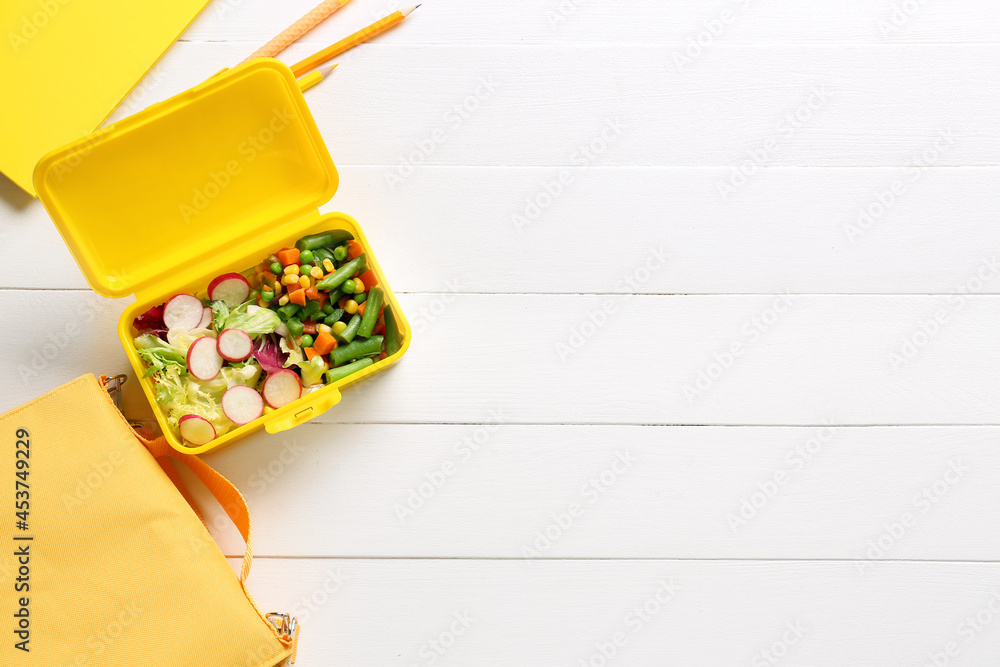 Lunch box with vegetables, bag and stationery on light wooden background