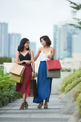 Sticker - Cheerful young women with shopping bags laughing and chatting when walking outdoors after buying new clothes in mall