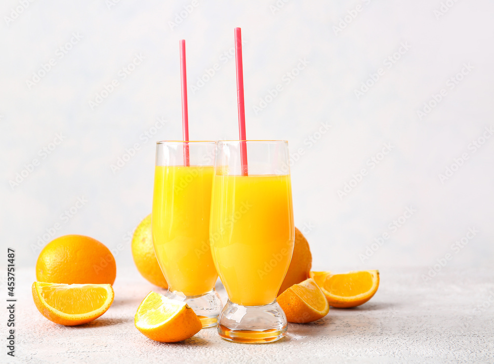 Glasses of tasty orange juice on light background