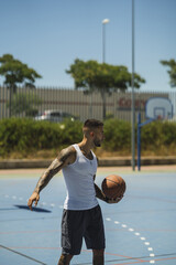 Wall Mural - Handsome caucasian basketball player with cool tattoos standing on the court with the ball