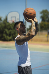 Wall Mural - Handsome caucasian basketball player with cool tattoos standing on the court throwing the ball up