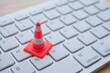 Maintenance, repair, under construction in computer system concept. Close up single orange white traffic warning cone or pylon on keyboard computer background with copy space.
