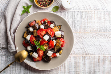 Poster - Summer salad with feta cheese, baked eggplant and fresh tomatoes, basil, olive oil.  Top view, light background.