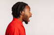 © khosrork - Side view portrait of bearded man with dreadlocks wearing red casual style T-shirt, standing with open mouth, being impressed of shocking news. Indoor studio shot isolated on gray background.