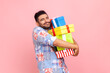 © khosrork - Happy satisfied man with beard wearing blue casual style shirt embracing stack of present boxes, keeping eyes closed, enjoying holiday. Indoor studio shot isolated on pink background.