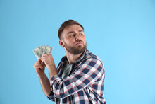 Greedy Young Man Hiding Money On Light Blue Background