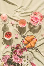Sunny Aesthetic Picnic Breakfast With Flowers Floating In Crystal Vases, Croissants With Tea From Rose Petals , Bouquet Of Flowers And Candles On Blanket. Top View. Outdoor
