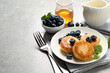 Delicious cottage cheese pancakes with blueberries, mint and honey on light grey table, space for text