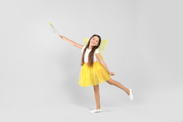 Canvas Print - Cute little girl in fairy costume with yellow wings and magic wand on light background