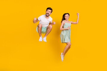 Wall Mural - Photo of crazy married couple raise fists jump achieve goal wear casual outfit isolated yellow color background