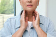 Mature woman doing thyroid self examination near window, closeup
