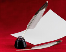 Quill Feather Pens With Ink Bottle And Sheet Of Writing Paper On A Red Background