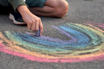 Kids paint outdoors. Boy drawing a rainbow colored chalk on the asphalt the playground