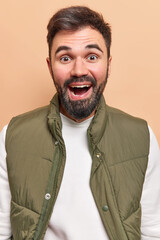 Wall Mural - Image of handsome bearded man smiles happily has positive expression feels satisfied hears excellent news wears white jumper with vest isolated over beige background. Human emotions concept.