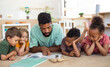 © Halfpoint - Group of small nursery school children with man teacher on floor indoors in classroom, reading book.