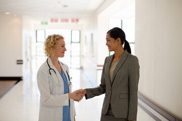 Wall Mural - Doctor and businesswoman handshaking in hospital corridor