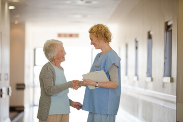 Nurse and senior patient shaking hands in hospital corridor