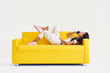 Smiling asian woman relax talking on cell lying on yellow couch on white background.