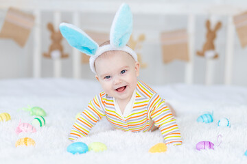 Wall Mural - baby boy with rabbit ears on his head lying on the bed with Easter eggs, cute funny smiling little baby. The concept of Easter.