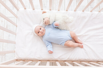 Wall Mural - baby in crib with teddy bear toy goes to bed or woke up in the morning, family and birth concept