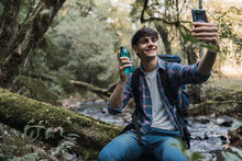 Male Traveler Drinking Water And Taking Photo During Trekking In Woods
