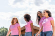 Cheerful multiethnic women with pink ribbons walking outdoors