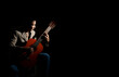 © Anucha - A young musician in a brown suit jacket an playing a classical guitar on the black background. Low Key portrait, copy space on the right.