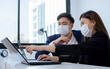 © Ann Rodchua - Two asian formal business man and woman wearing face mask to protect virus while working, typing, discussing with confidence and using laptop in the modern office.