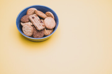 Poster - Vertical shot of organic biscuits in a blue bowl on yellow background