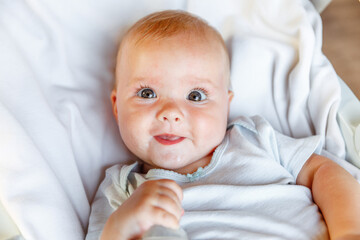 Cute little newborn girl with smiling face looking at camera on white background. Infant baby resting playing lying down on crib bed at home. Motherhood happy child concept