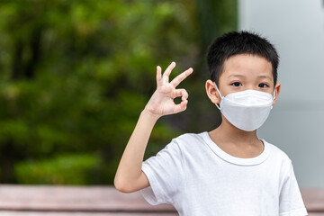 Cute smiling little child boy making OK gesture. Happy Asian boy in white t-shirt showing ok hand sign. A kid wearing face mask protection virus concept.