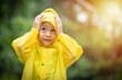A boy wearing a yellow raincoat. Happy Asian little child having fun playing with the raindrops. A boy looking up at the sky and enjoying rainfall.