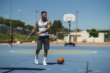 Wall Mural - Young caucasian guy with cool tattoos standing on the basketball court with a ball