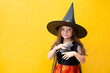 © Анна Брусницына - Halloween. A funny girl in a witch costume holds a rat. Yellow background, space for text. Emotional portrait.