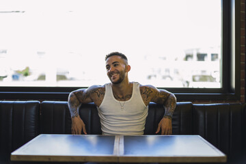 Canvas Print - Young smiling caucasian guy with cool tattoos sitting in the cafe