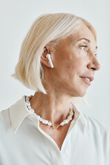 Wall Mural - Vertical side view portrait of modern mature woman with wireless earphones in focus