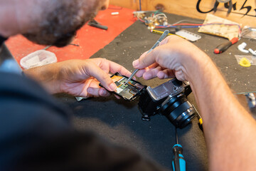 Poster - Shot of the Hispanic man fixing a camera in the service shop with its precision tweezers.