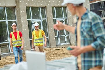 Wall Mural - Serious construction workers in reflective waistcoats approaching their colleague