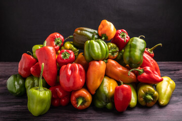 pile of yellow red and green bell peppers on dark background