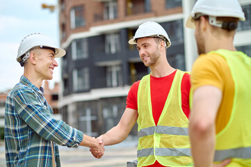 Wall Mural - Handsome bearded Caucasian construction worker shaking his colleague hand