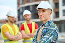 Three Men In Protective Helmets Standing On The Building Site