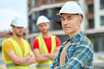 Poster - Three men in protective helmets standing on the building site