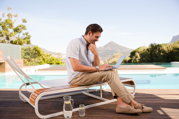 Wall Mural - Man using laptop on lounge chair at poolside