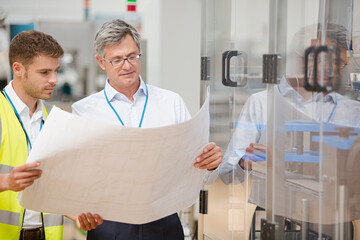 Supervisor and worker reading blueprints in factory