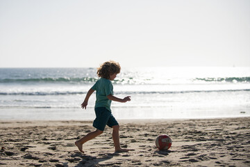 Wall Mural - Little boy child play football on coast of sea beach. Summer kids sports.