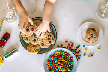 Funny male brothers eat cookies with round multi-colored sweets m&m and drink milk. Top view.