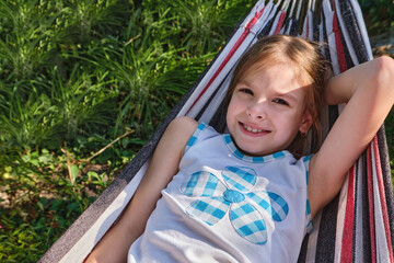 a happy little girl lies in a hammock in the garden in the summer. a child in a hammock during the h