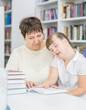 Senior woman helps to girl with syndrome doing homework at a school. Education for disabled children concept